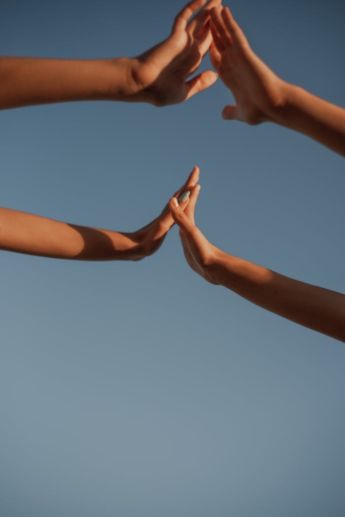 Multiple hands reaching together against a clear blue sky, symbolizing unity and teamwork.